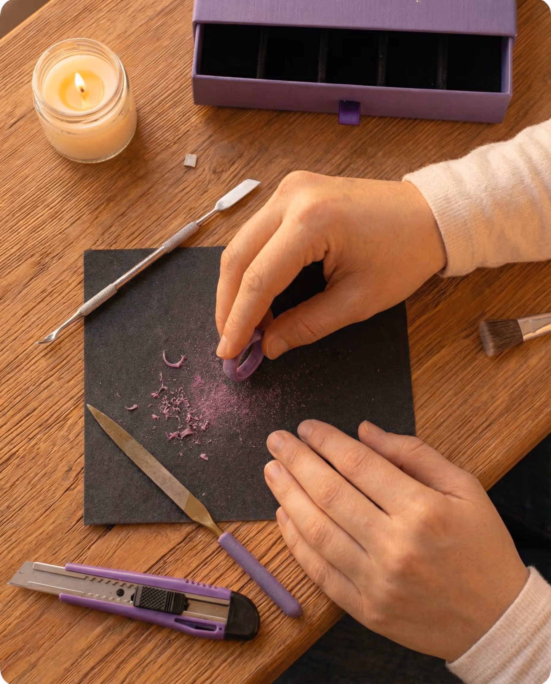 Overhead view of ring-carving tools on wooden table with candle